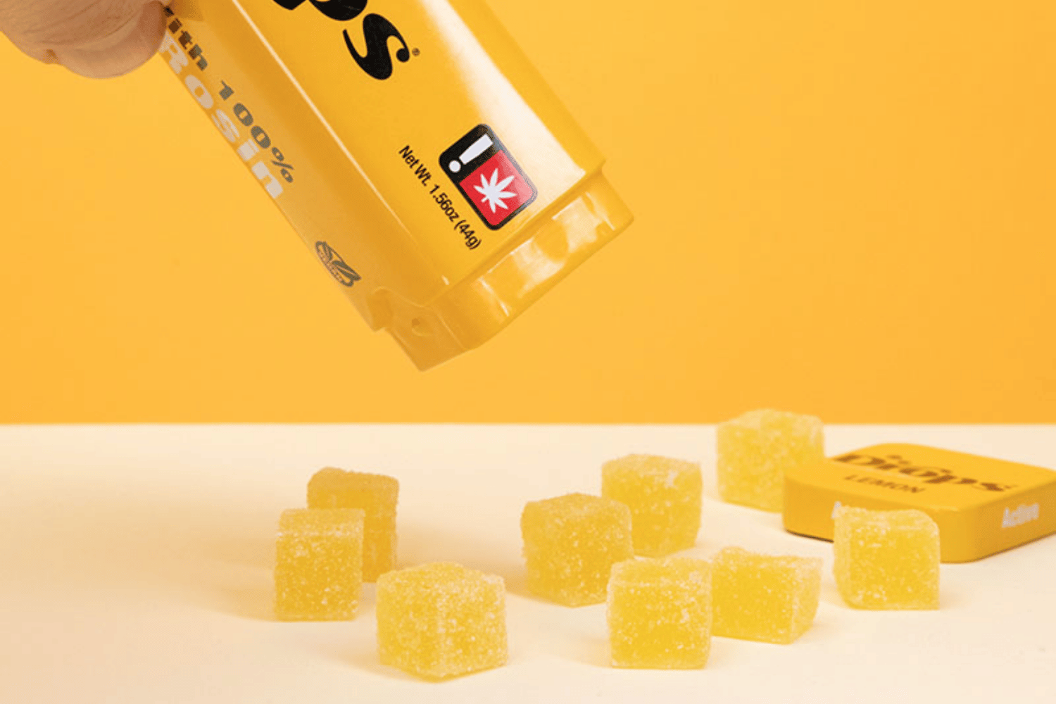 Close-up of yellow cannabis-infused Drops gummies spilled from their packaging, showcasing their vibrant color and texture.