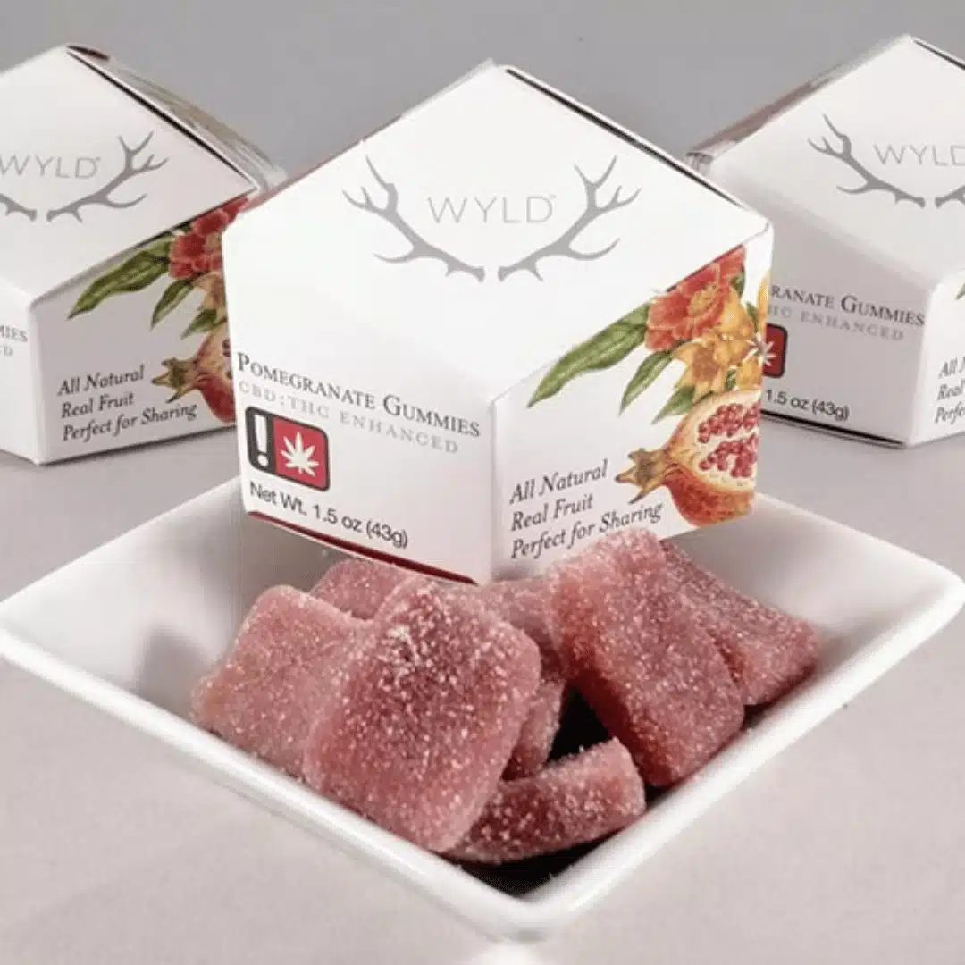 Wyld Pomegranate cannabis-infused gummies in hybrid formulation, displayed in a bowl with elegant packaging featuring fruit illustrations.