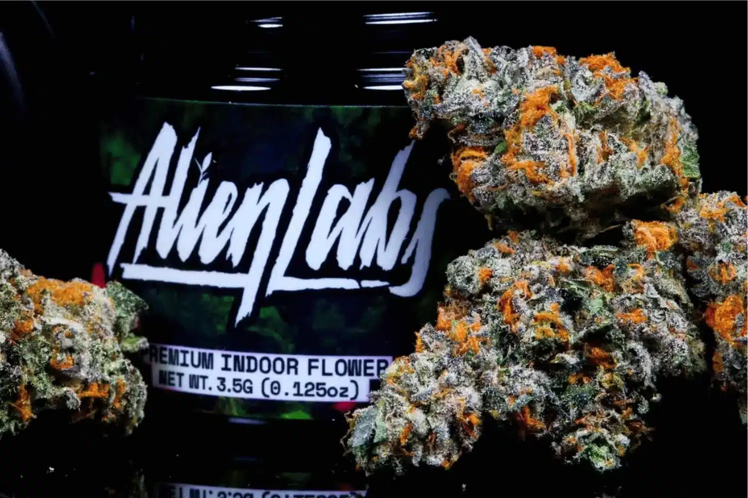 Alien Labs branded jar of premium indoor cannabis flower with dense, vibrant nugs showcasing orange hairs and frosty trichomes.