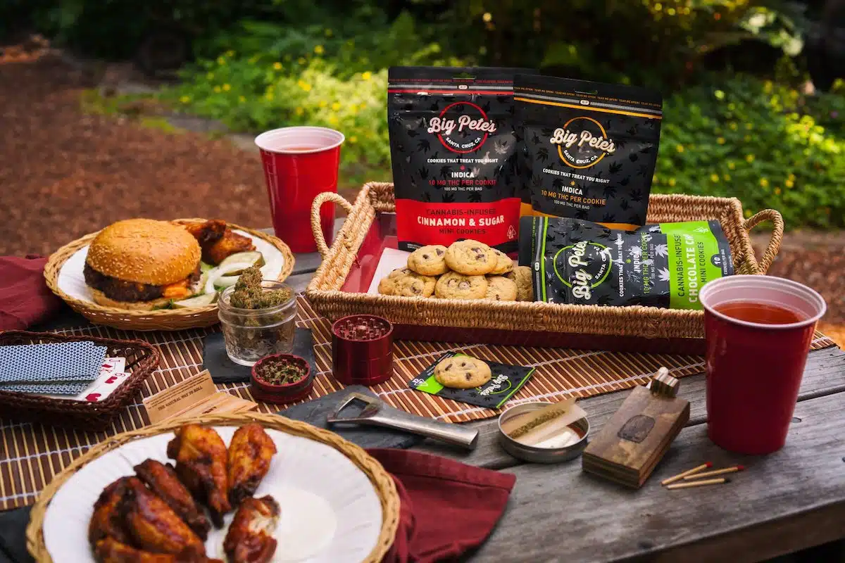 Big Pete’s cannabis-infused cookies displayed on an outdoor picnic table alongside a burger, wings, and a jar of cannabis buds