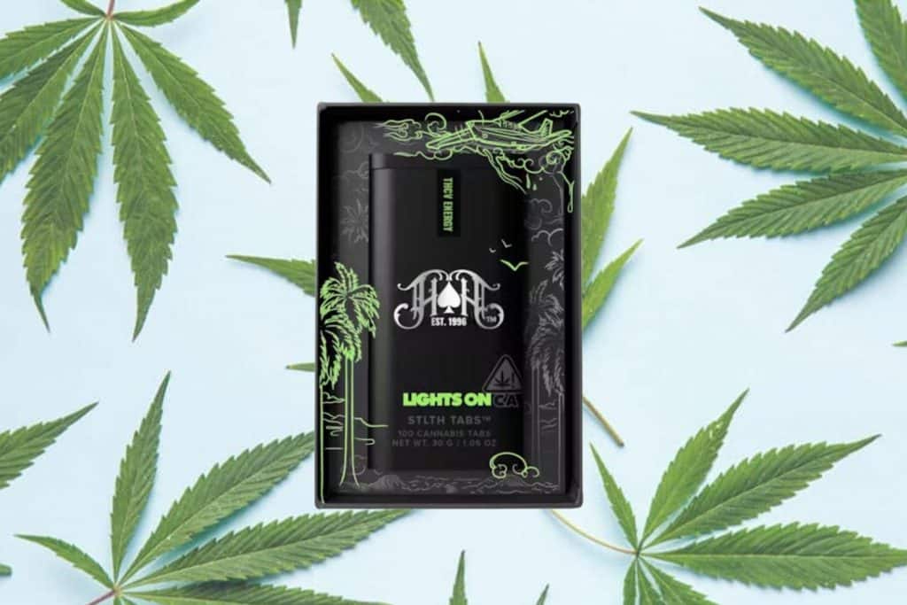 Heavy Hitters Lights On THCV cannabis tablets in a sleek black case with green detailing, placed on a light blue background with cannabis leaves.