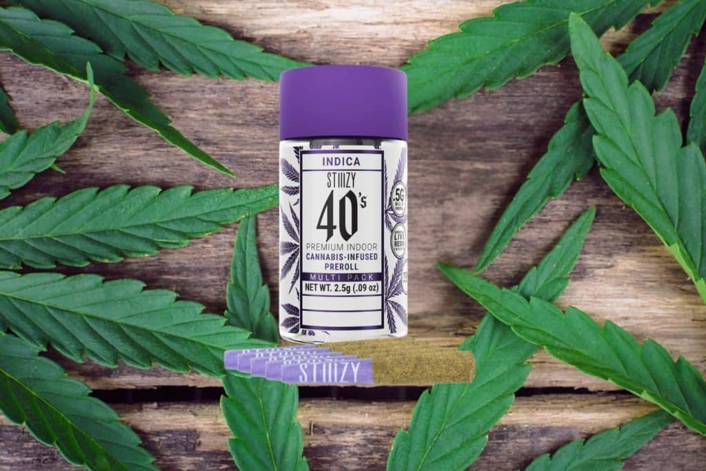 Stiiizy 40s Indica pre-roll multipack with purple packaging and cannabis-infused pre-rolls, set on a wooden surface with cannabis leaves.